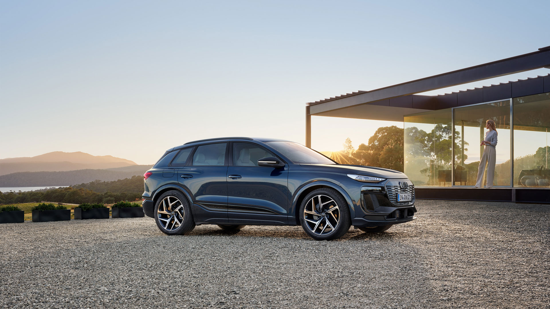 Three-quarter side view of the Audi Q6 e-tron parked next to a modern house.